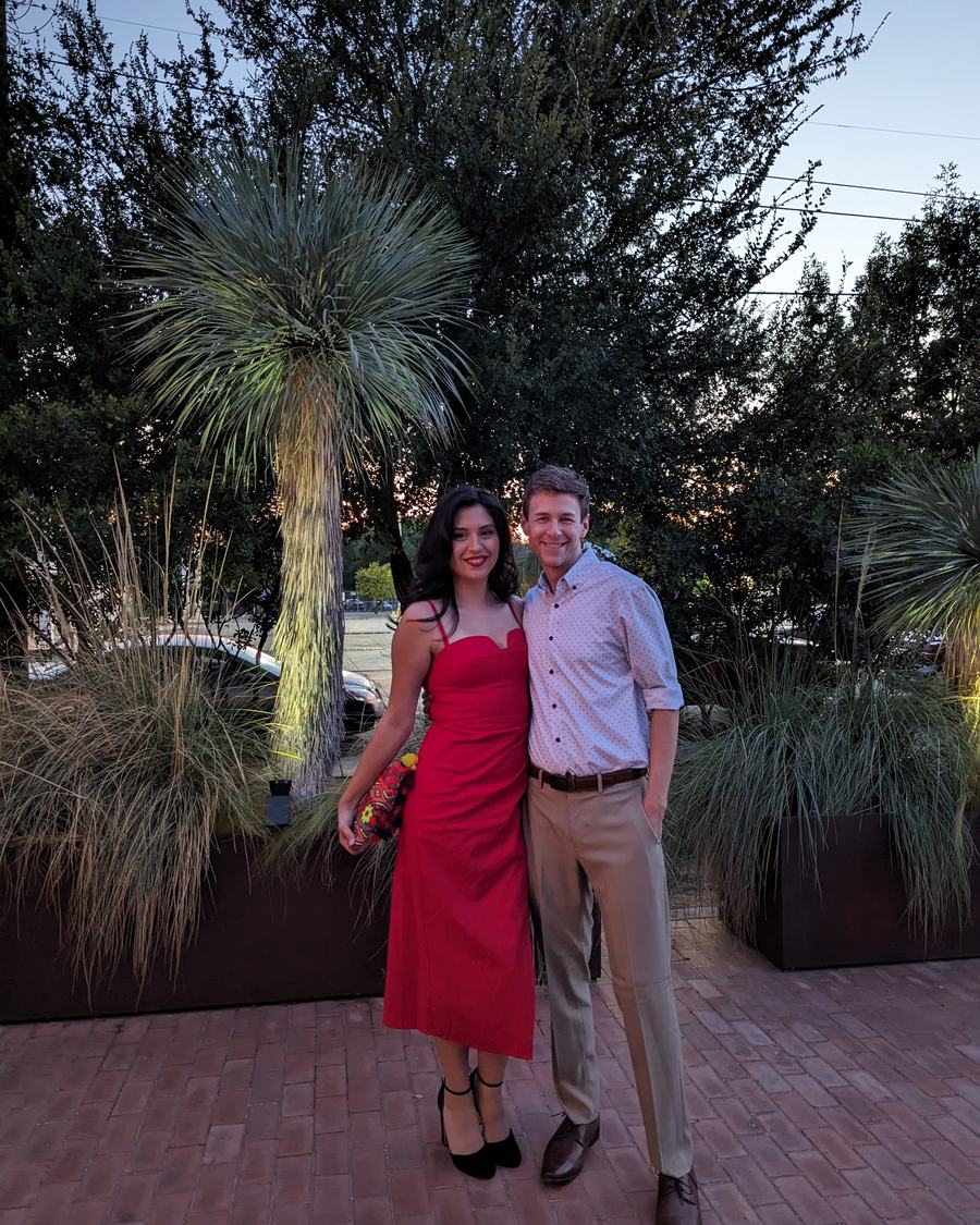 Megan in a red dress and Tyler dressed up, standing together in a garden